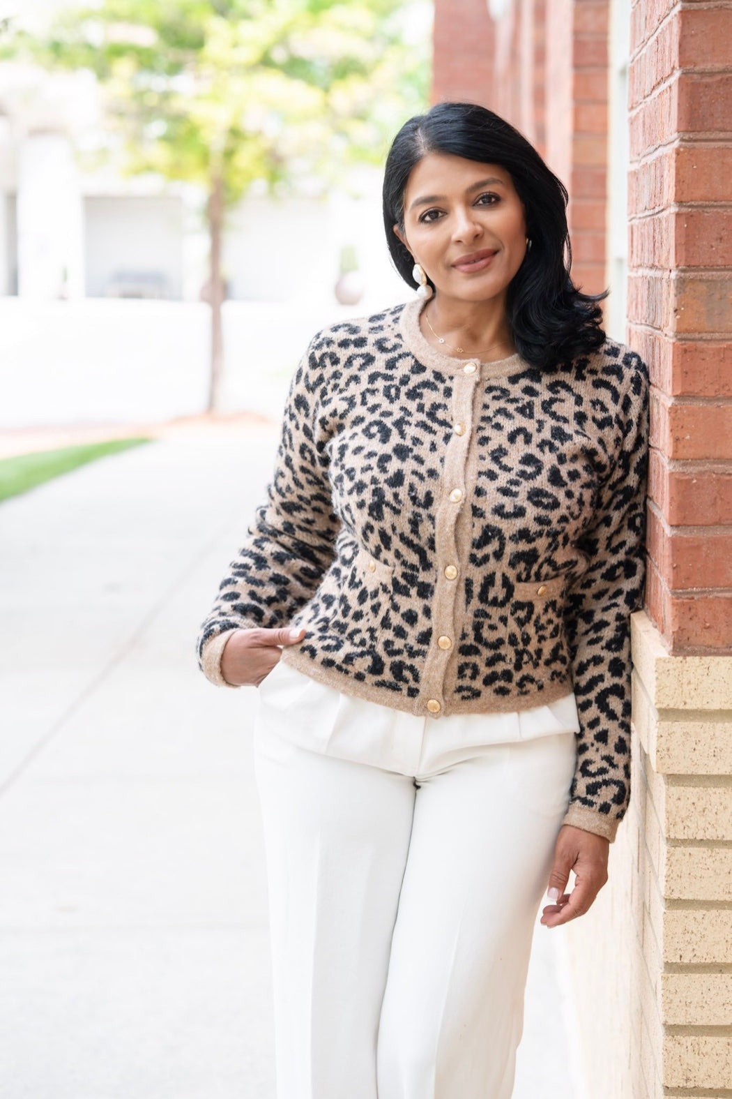 Priti Patel, founder of Le Petit Spa, in a leopard print cardigan leaning against a brick wall