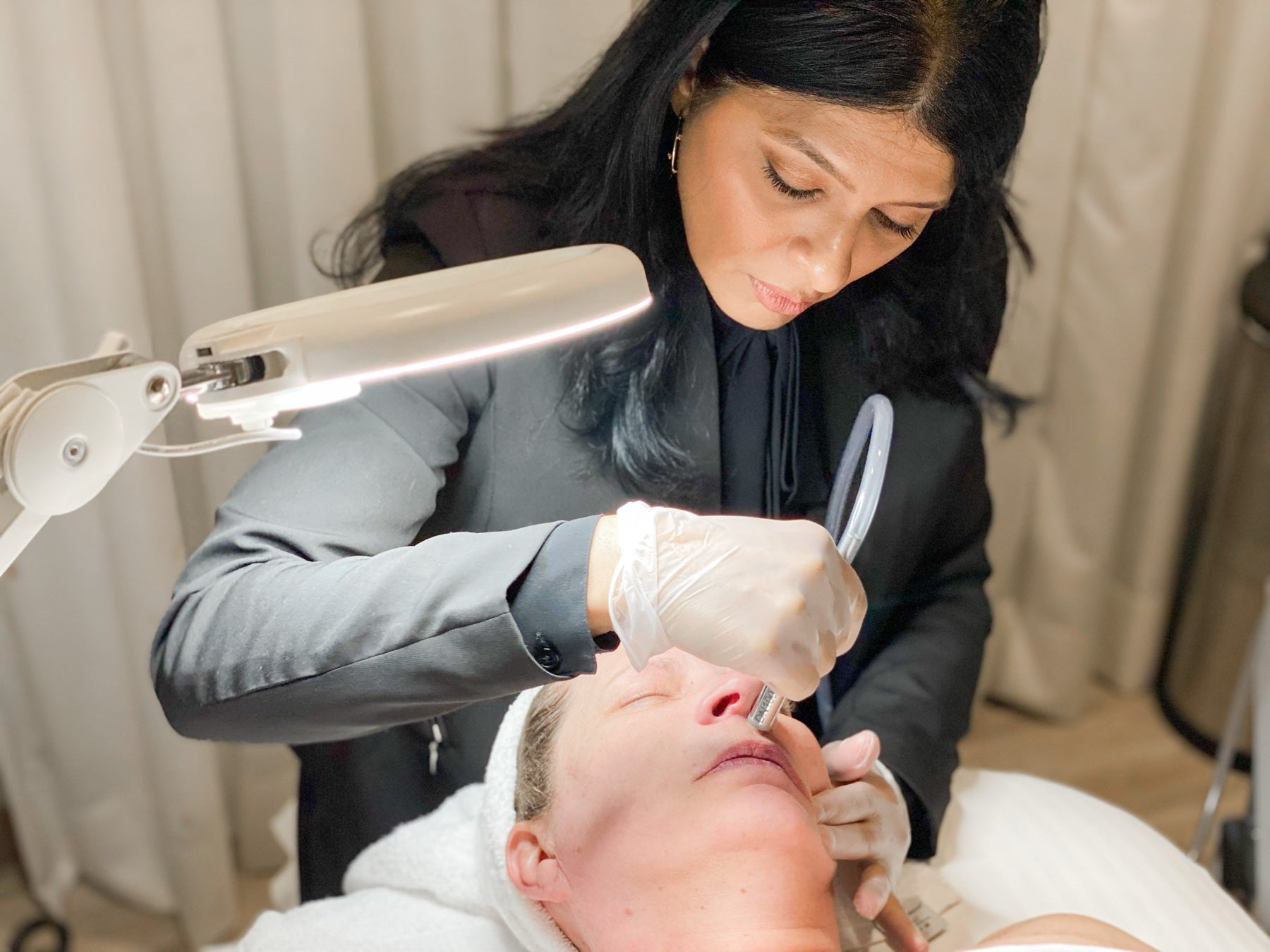 Priti Patel performing a facial treatment under a magnifying lamp at Le Petit Spa