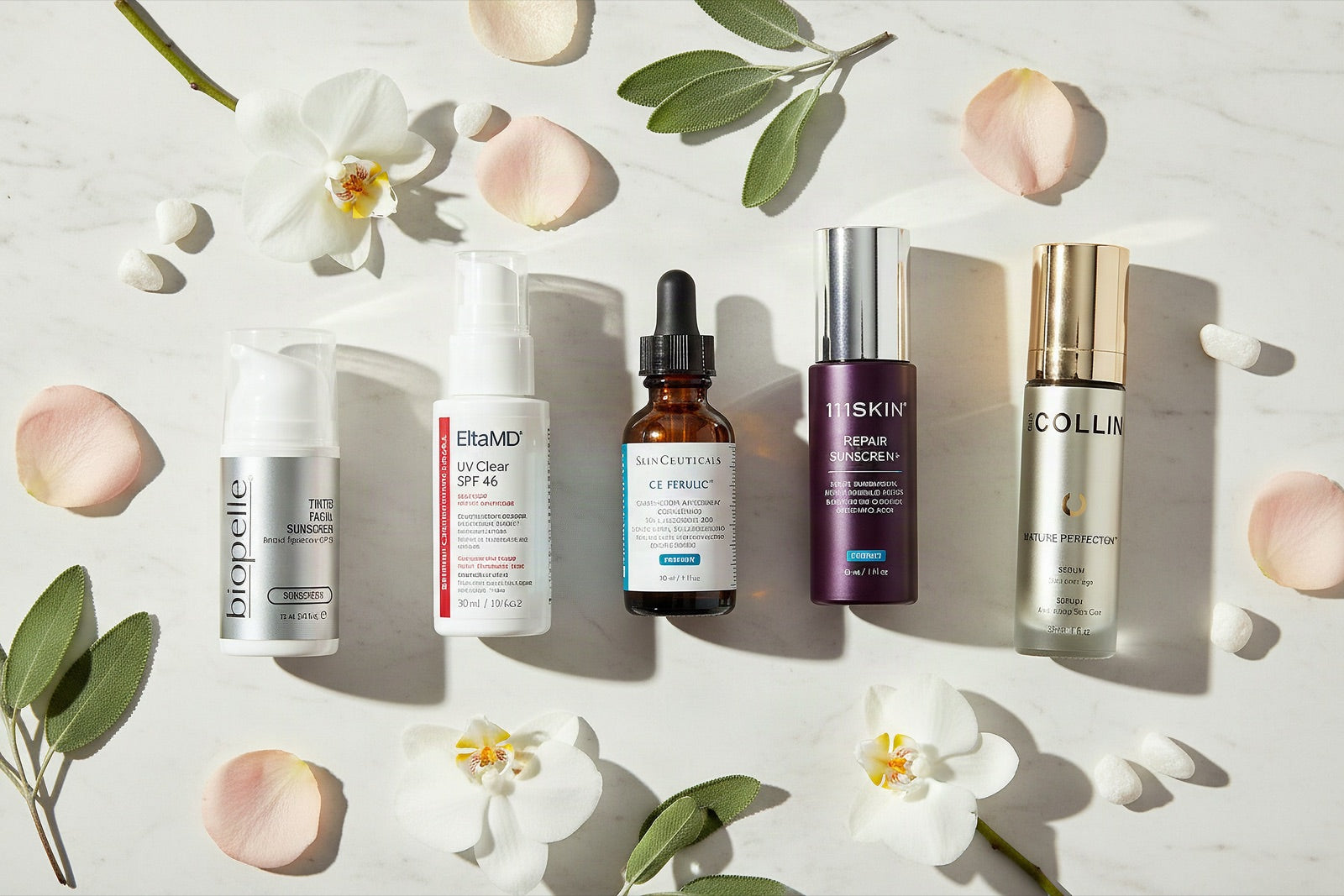 Biopelle, EltaMD, SkinCeuticals, 111SKIN and Colbert MD serums laid out on marble with orchids and rose petals
