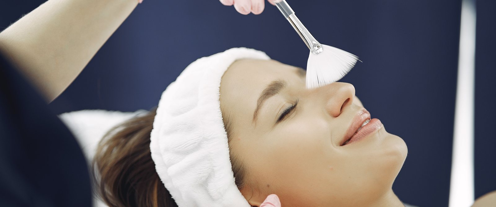 A fan brush laying a treatment mask across a client's cheek during a facial.
