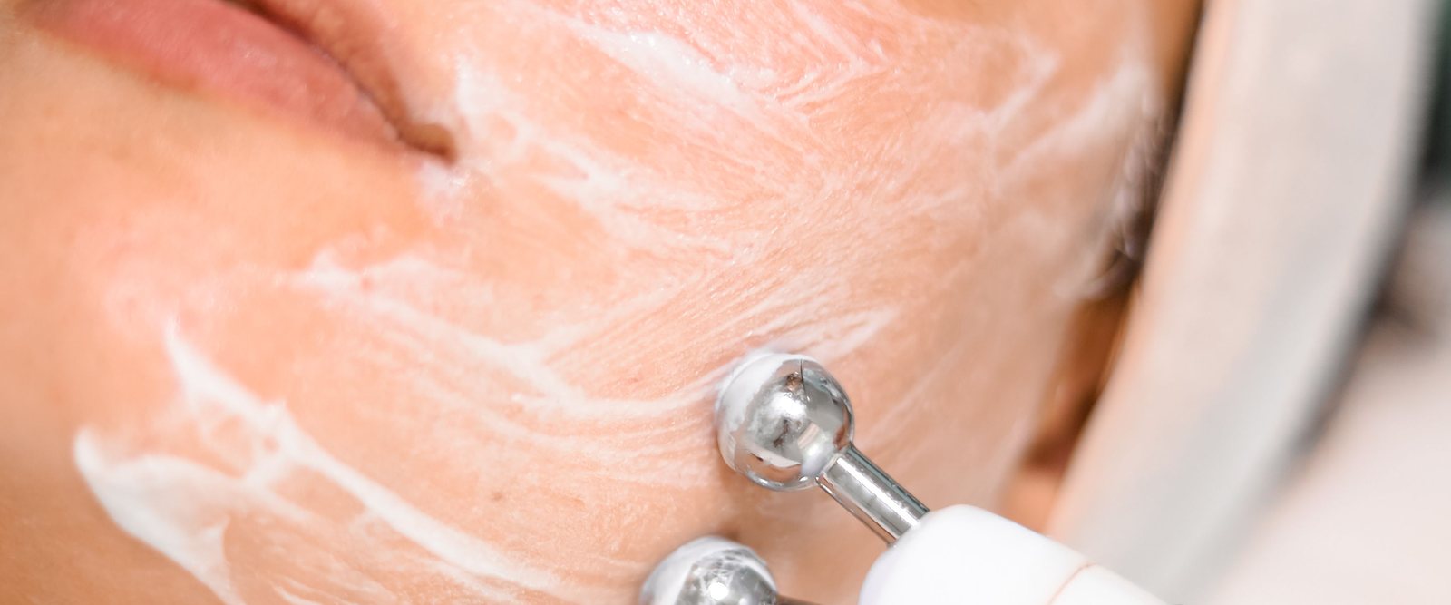Twin chrome microcurrent probes gliding over a cheek through conductive cream.