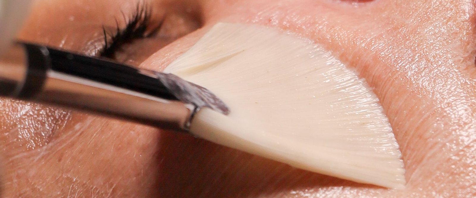 A peel solution brushed across a client's cheek with a soft fan brush.