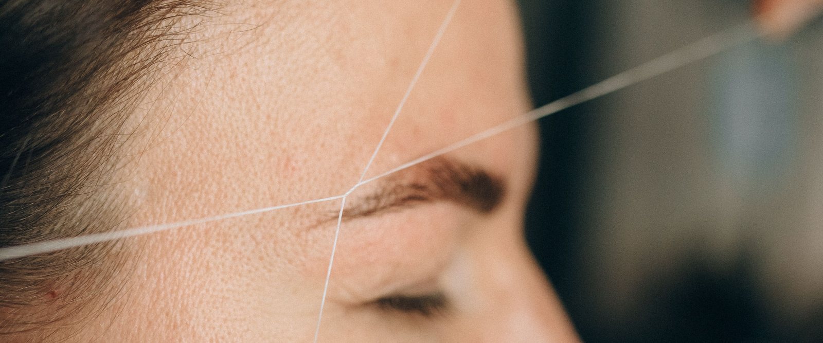 A cotton thread drawn taut across a client's brow during threading.
