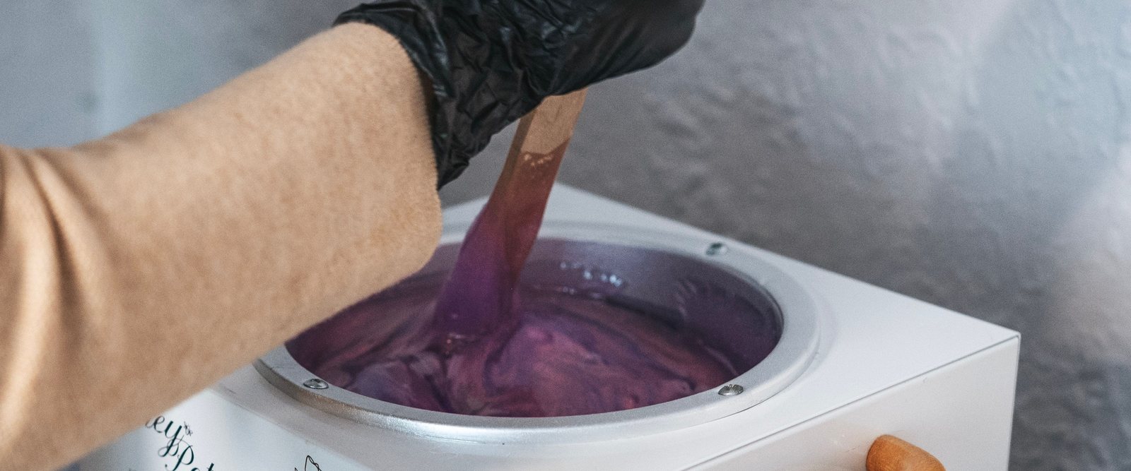 Warm wax lifted onto a wooden spatula from a heated wax pot.